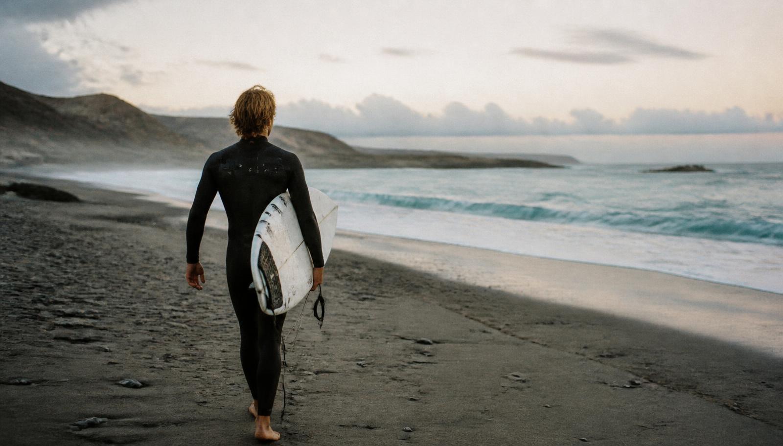 Surfer walking along a quiet beach at dawn with a surfboard